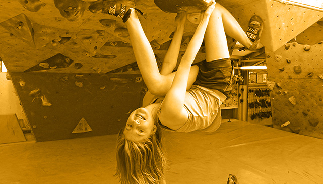Ein Mädchen hängt kopfüber an einer Boulderwand.